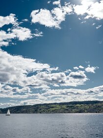 Image of sailboat with land behind it and cloudy sky