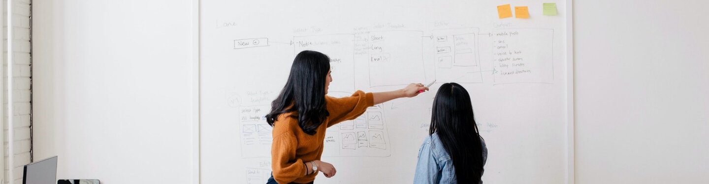 2 woman discussing a plan written out on a whiteboard